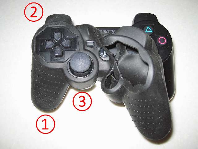 BeryKoKo PlayStation3 DUALSHOCK3 対応 ゴムカバー を DUALSHOCK3 に装着作業、アナログスティックや L・R ボタンなどのアタッチメントが装着されている場合は事前に取り外しておく。コントローラー左側持ち手をゴムカバーを奥まで入れながら（1）、L1・L2 ボタン側にゴムカバーを被せて（2）、ゴムカバーのアナログスティックの穴に左アナログスティックを通す（3）。